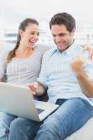 Excited couple sitting on the couch using laptop together