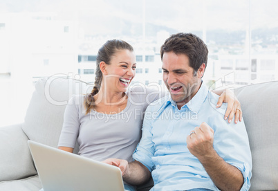Excited couple sitting on the sofa using laptop together