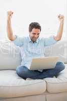 Cheering man using laptop sitting on sofa