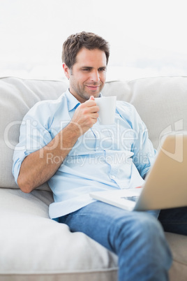 Content man using laptop sitting on sofa having a coffee