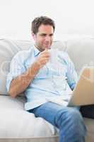 Content man using laptop sitting on sofa having a coffee