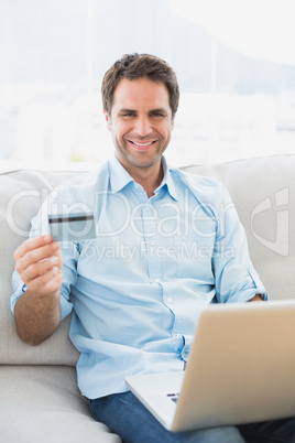 Smiling man using laptop sitting on sofa shopping online