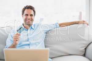 Happy man using laptop sitting on sofa shopping online