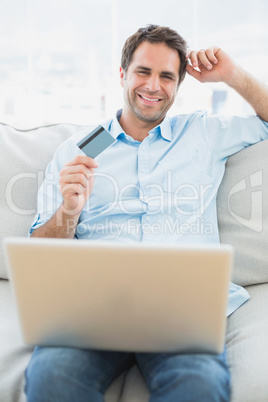 Cheerful man using laptop sitting on sofa shopping online