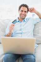 Cheerful man using laptop sitting on sofa shopping online