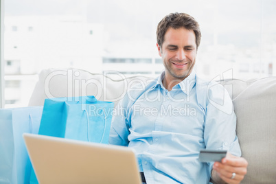 Handsome man using laptop sitting on sofa shopping online