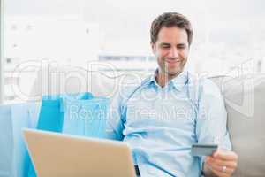 Handsome man using laptop sitting on sofa shopping online