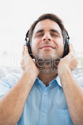 Content man sitting on sofa listening to music with eyes closed