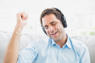 Singing man sitting on sofa listening to music with eyes closed