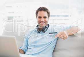Happy handsome man sitting on sofa online shopping with laptop