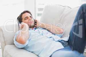 Happy handsome man lying on sofa listening to music