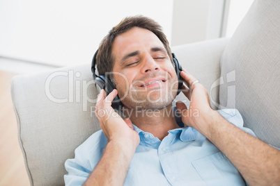 Smiling handsome man lying on sofa listening to music