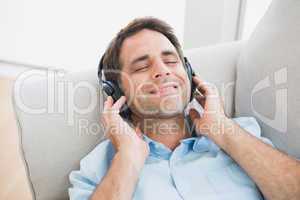 Smiling handsome man lying on sofa listening to music