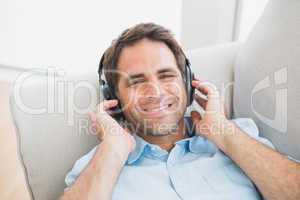 Smiling handsome man lying on sofa listening to music looking at