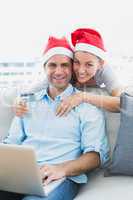 Happy couple in santa hats shopping online with laptop