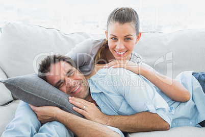 Cheerful couple relaxing on their sofa smiling at camera