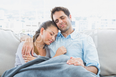 Cheerful couple relaxing on their sofa under blanket