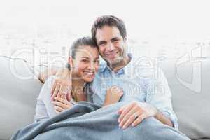 Cheerful couple relaxing on their sofa smiling at camera under b