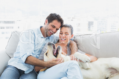 Happy couple petting their yellow labrador on the couch