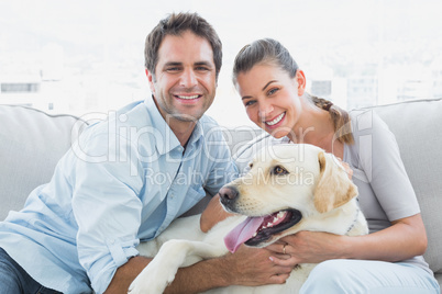 Smiling couple petting their yellow labrador on the couch