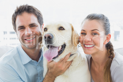 Happy couple rubbing their yellow labrador on the couch