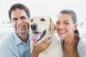 Happy couple rubbing their yellow labrador on the couch