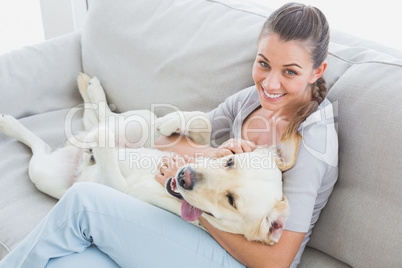 Happy woman rubbing her yellow labrador on the couch