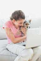 Happy woman holding her yorkshire terrier on the couch using lap