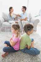 Siblings sitting back to back while parents are arguing