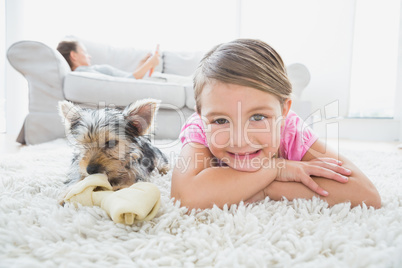 Little girl lying on rug with yorkshire terrier smiling at camer