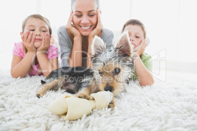 Siblings lying on rug looking at their yorkshire terrier with mo