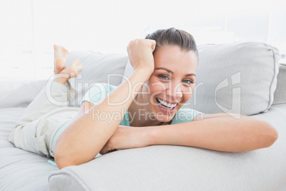 Cheerful woman lying on couch smiling at camera