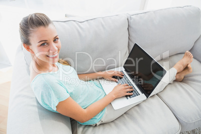 Happy woman sitting on couch using her laptop smiling up at came