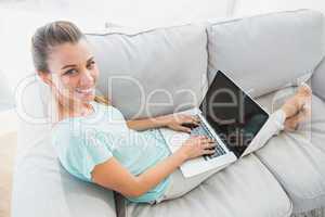 Happy woman sitting on couch using her laptop smiling up at came