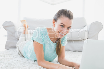 Smiling woman lying on rug using her laptop