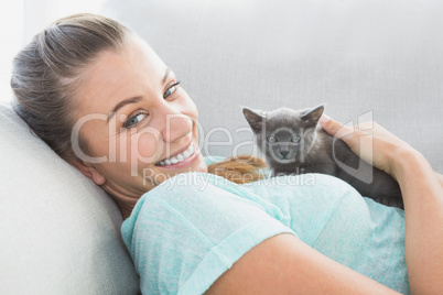 Cheerful woman lying on sofa cuddling a grey kitten