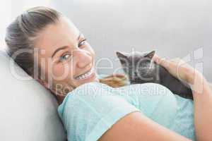 Cheerful woman lying on sofa cuddling a grey kitten