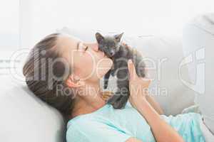 Cheerful woman lying on sofa kissing a grey kitten