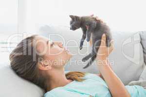 Cheerful woman lying on sofa holding a grey kitten