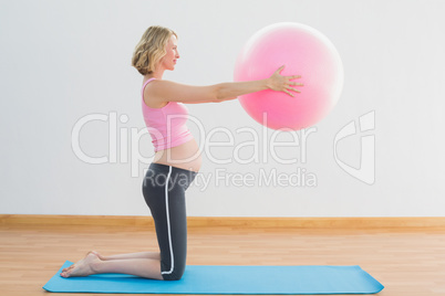 Cheerful blonde pregnant woman lifting exercise ball