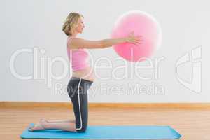 Cheerful blonde pregnant woman lifting exercise ball