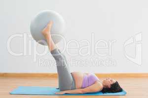 Happy pregnant woman lifting exercise ball with legs