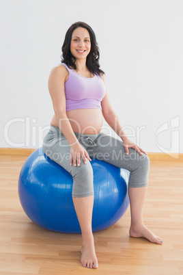 Pregnant woman sitting on blue exercise ball smiling at camera