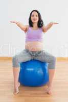 Pregnant woman sitting on blue exercise ball with arms outstretc