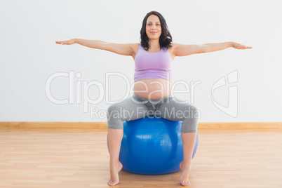 Pregnant woman sitting on blue exercise ball with arms out