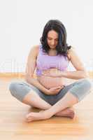 Pregnant woman sitting on floor holding belly