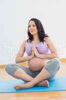 Pregnant woman sitting on mat in lotus pose smiling