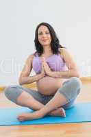 Pregnant woman sitting on blue mat in lotus pose smiling at came