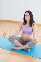 Smiling pregnant woman sitting on blue mat in lotus pose