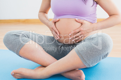 Pregnant woman sitting on mat in touching her belly